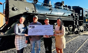 Two F&M Trust and two East Broad Top Railroad employees posing with a large check in front of a steam-powered train.