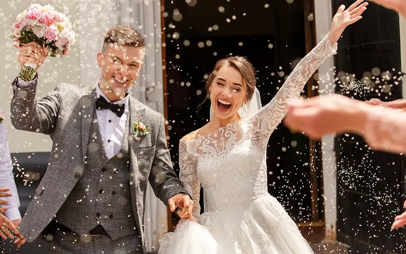 celebratory rice being tossed at young happy couple dressed in wedding attire