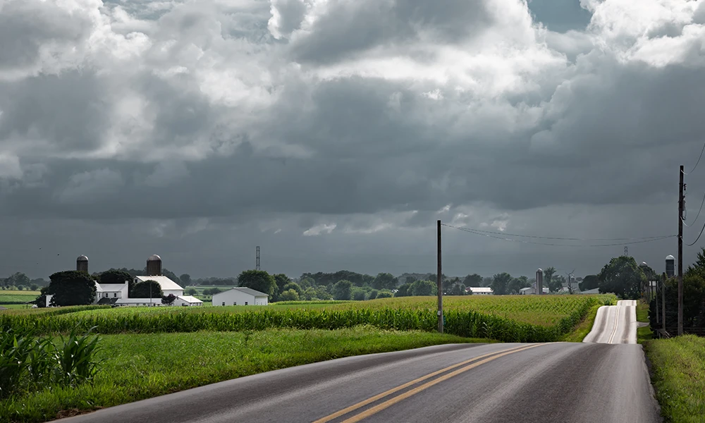 Country road with corn fields and a thunderstorm in the distance