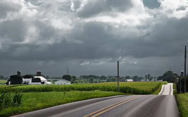Country road with corn fields and a thunderstorm in the distance