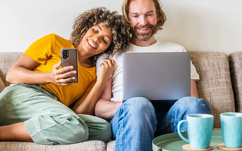 Young couple using computer laptop and smart mobile phone sitting on the sofa at home