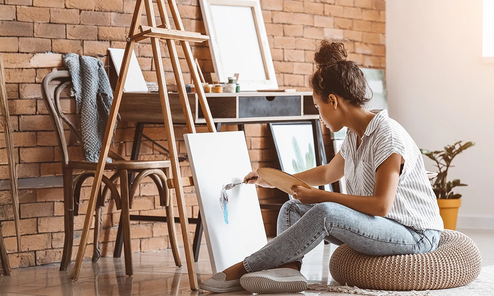 woman sitting casually on the floor painting a canvas 