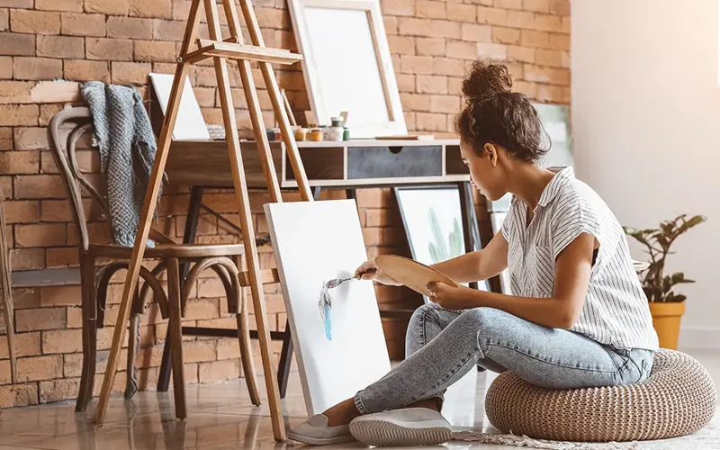 woman sitting casually on the floor painting a canvas 