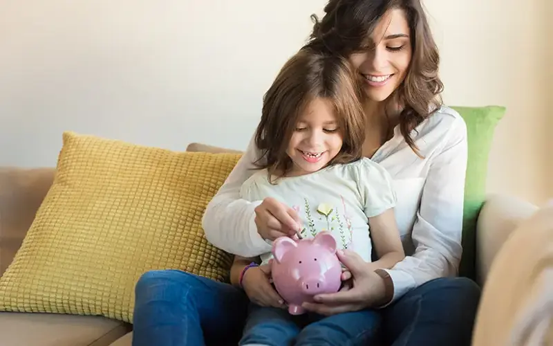 Mother holding daughter using piggy bank