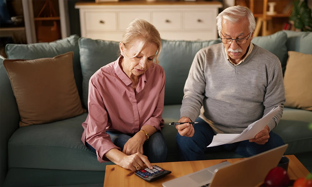 an older married couple using a calculator and reviewing finances