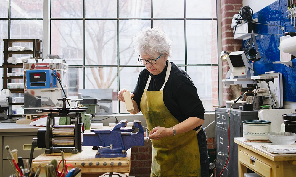 older woman using vise grip on a bench at work