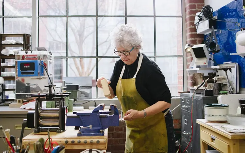 older woman using vise grip on a bench at work