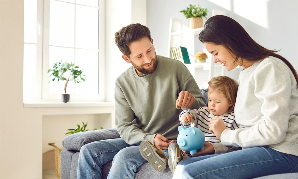 parents showing toddler how to put coins in a piggy bank