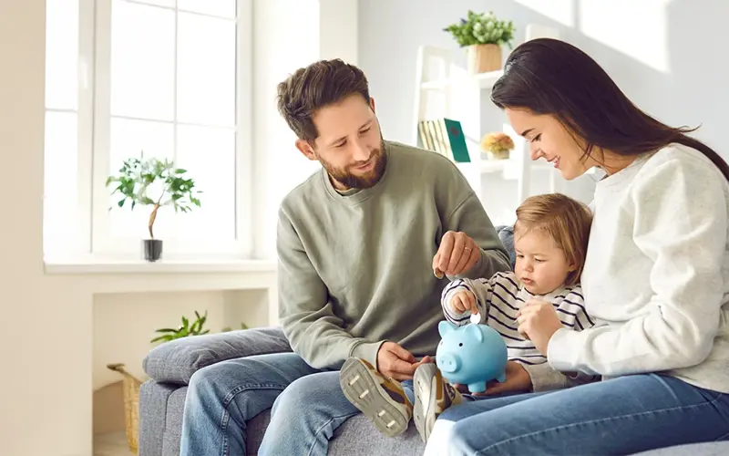 parents showing toddler how to put coins in a piggy bank