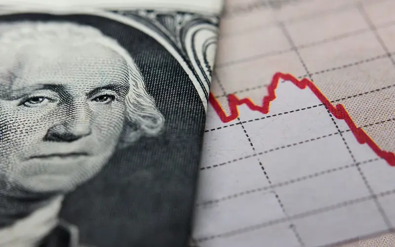 Washington's face on a dollar bill next to a paper showing a rate that is dropping