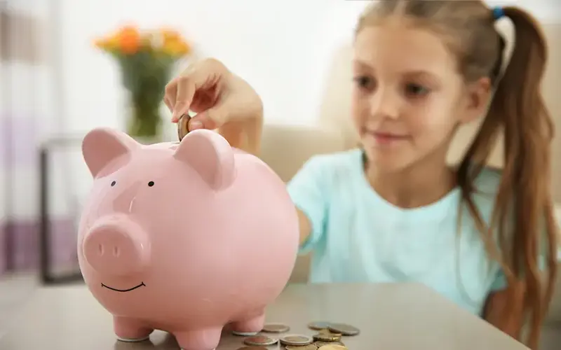 Young girl adding putting coins into a piggy bank