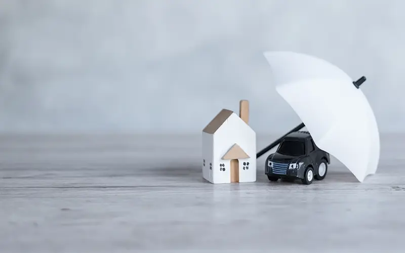 toy representatives of house and car with an umbrella protecting both