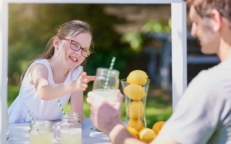 young girl hands glass of lemonade to a buyer at her stand