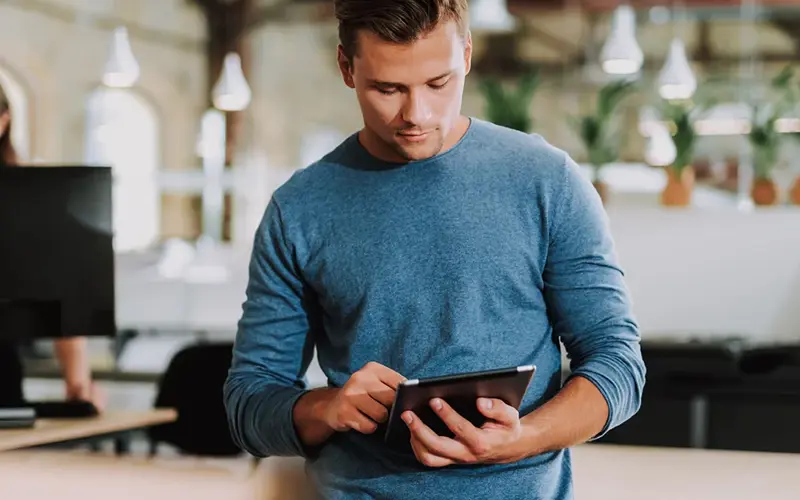 Young man standing in the office while using his tablet