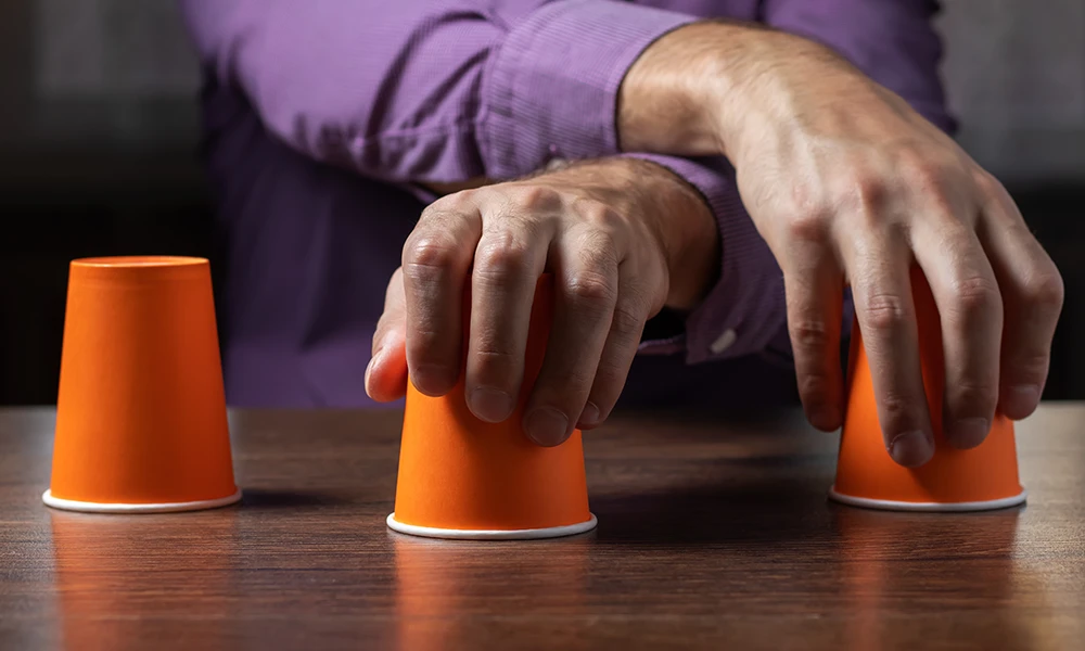 hands holding upside down cups representing three-shell game