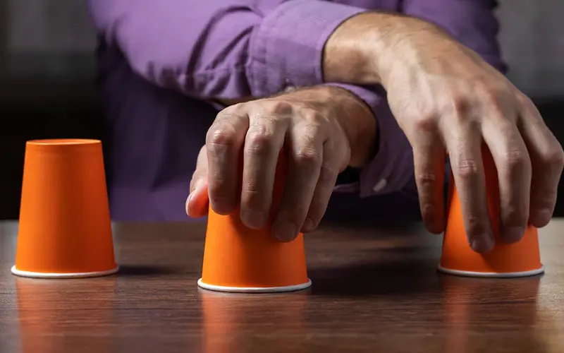 hands holding upside down cups representing three-shell game