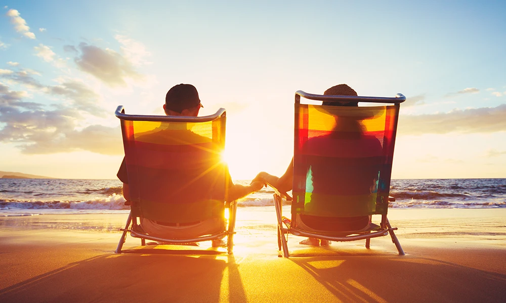 older couple holding hands while sitting on a beach