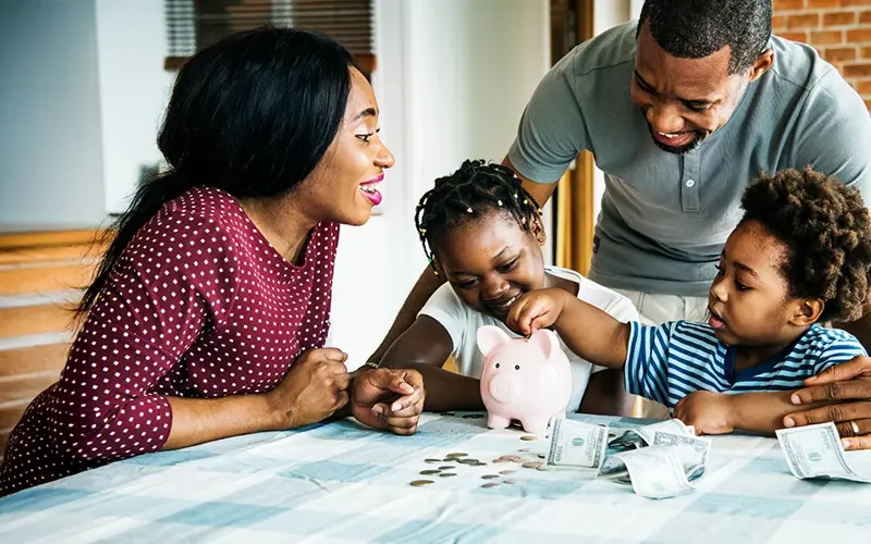 parents encouraging their young kids to put money in a piggy bank