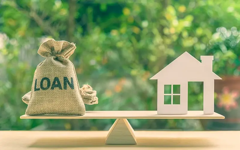 a balancing board with a bag of money labelled loan and on the other end a home