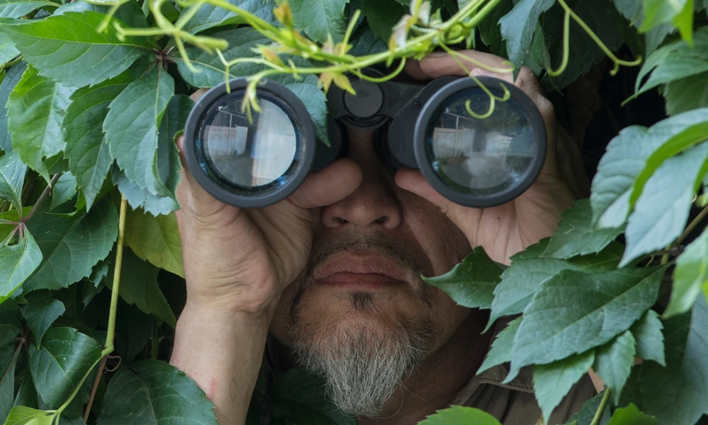 man hiding in bush with binoculars