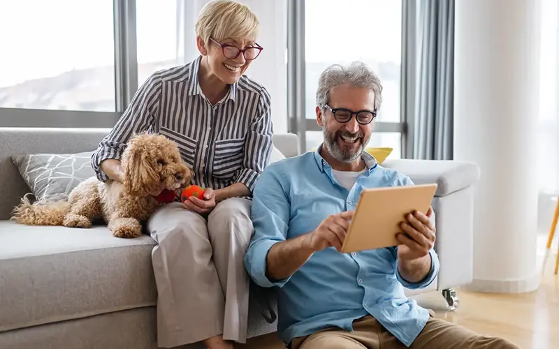 Beautiful happy mature couple is using a digital tablet, talking and smiling at home 