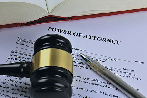 An image of a gavel and pen laying on top of Power of Attorney forms.