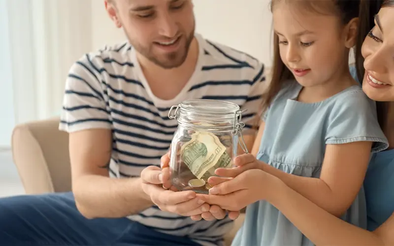 parents with young daughter holding a jar full of money