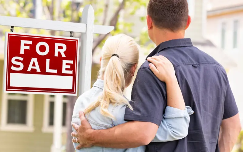 Couple embracing aside a house for sale sign