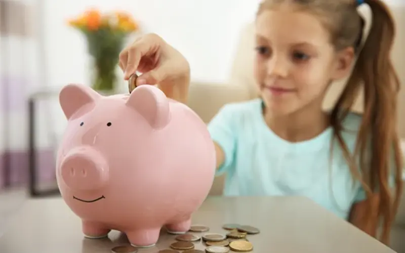 Young girl putting money in a piggy bank