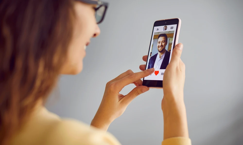 woman smiling at a picture of man on her phone with a heart icon 