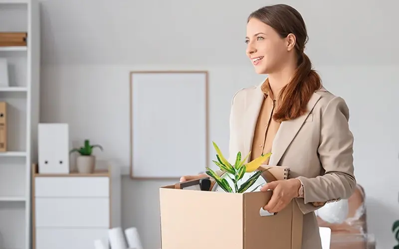 a business woman smiling as she carries a box of things into her new office